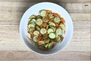 Cucumber and grated carrot salad in a white bowl on a wooden table. Fresh, healthy, and nutritious dish.